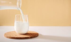 Pouring milk in glass from a bottle on a light neutral background
