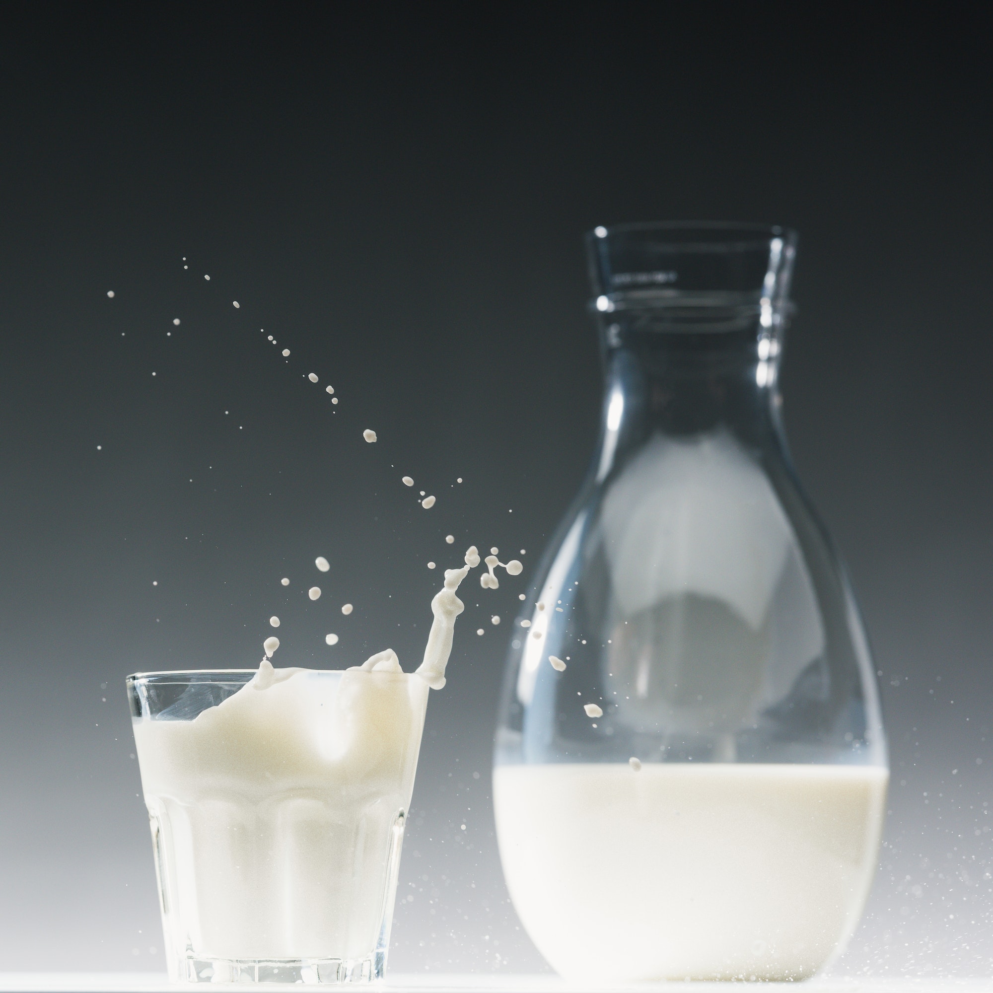 Glass of milk with splashes in front of milk bottle